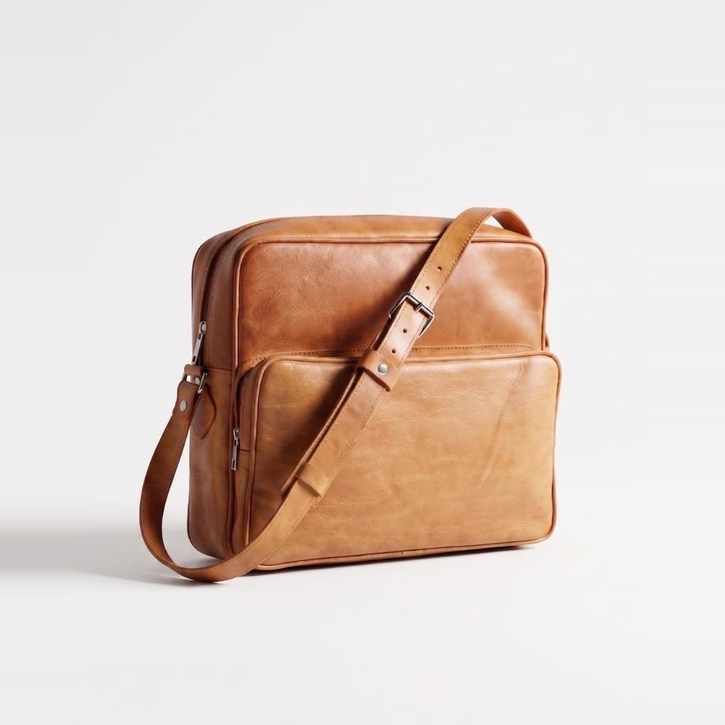 A tan leather messenger bag with a front pocket and an adjustable shoulder strap.