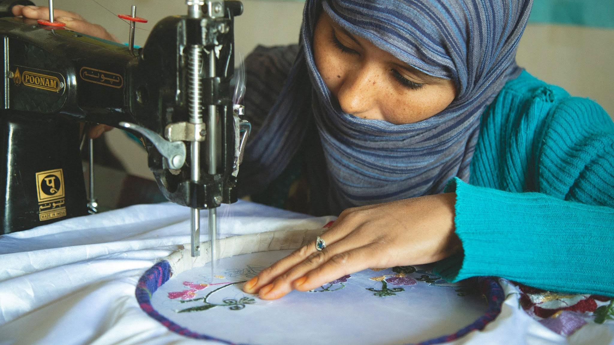 A woman embroidering flowers on white fabric at a sewing machine.