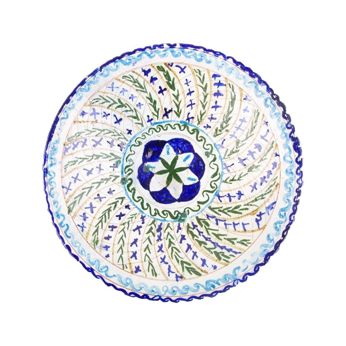 A round white ceramic plate painted with blue and green leaf strokes around a blue star centre.