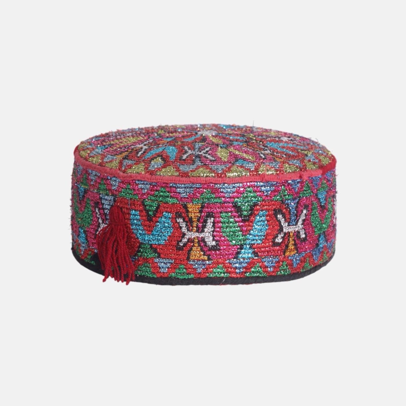 A round cap densely embroidered in red, blue and green geometric patterns with a red tassel.