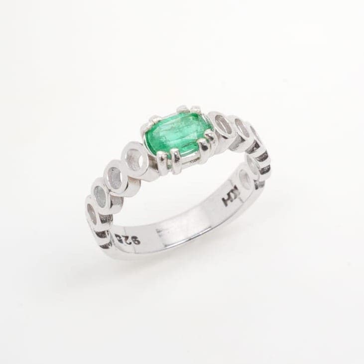 A silver ring set with an oval green emerald on a band of linked ovals.