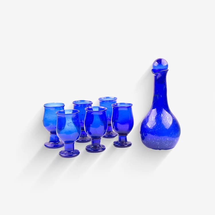 A cobalt blue glass carafe with a round stopper, beside six matching stemmed glasses.