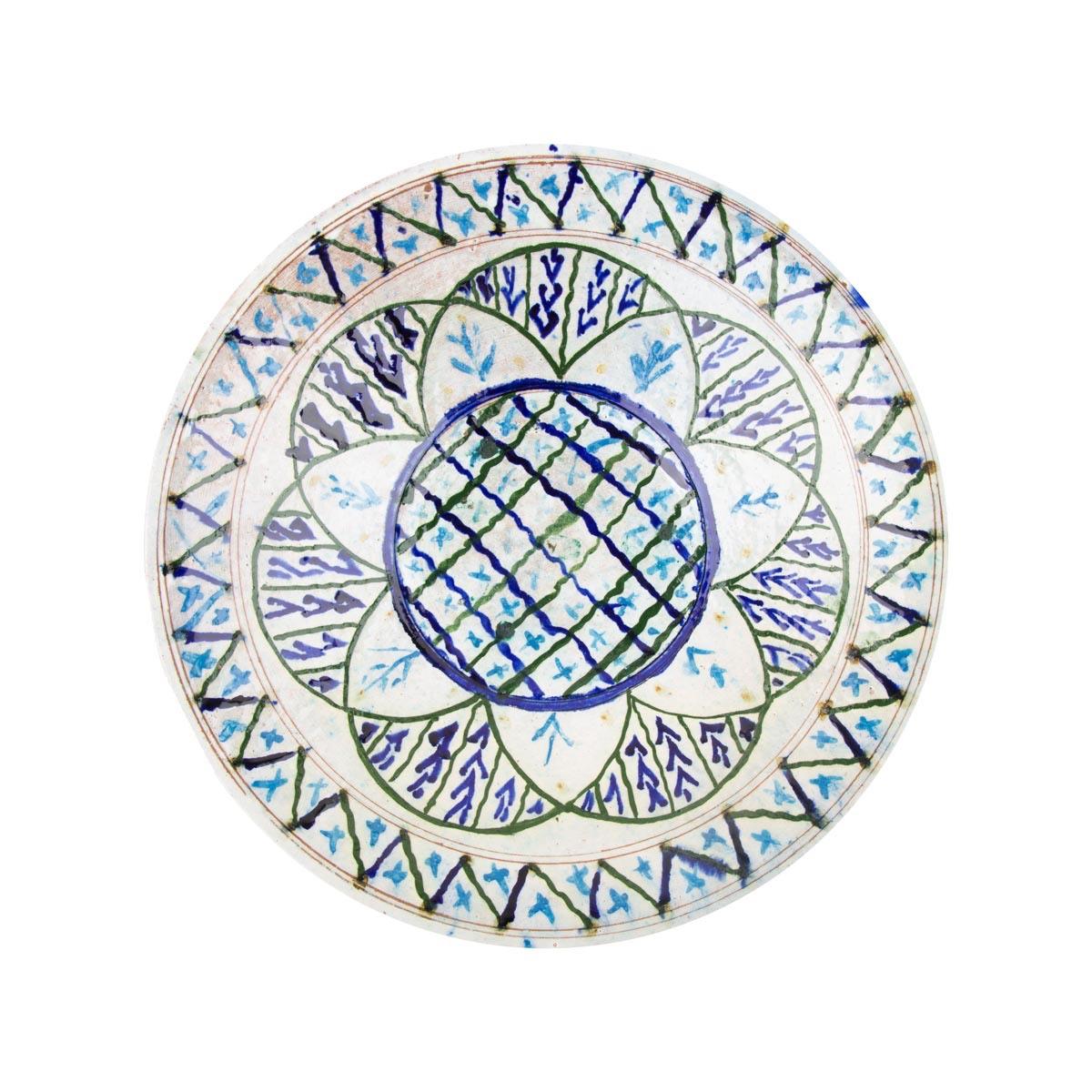 A white ceramic plate painted with a blue lattice centre, green petals and a zigzag border.