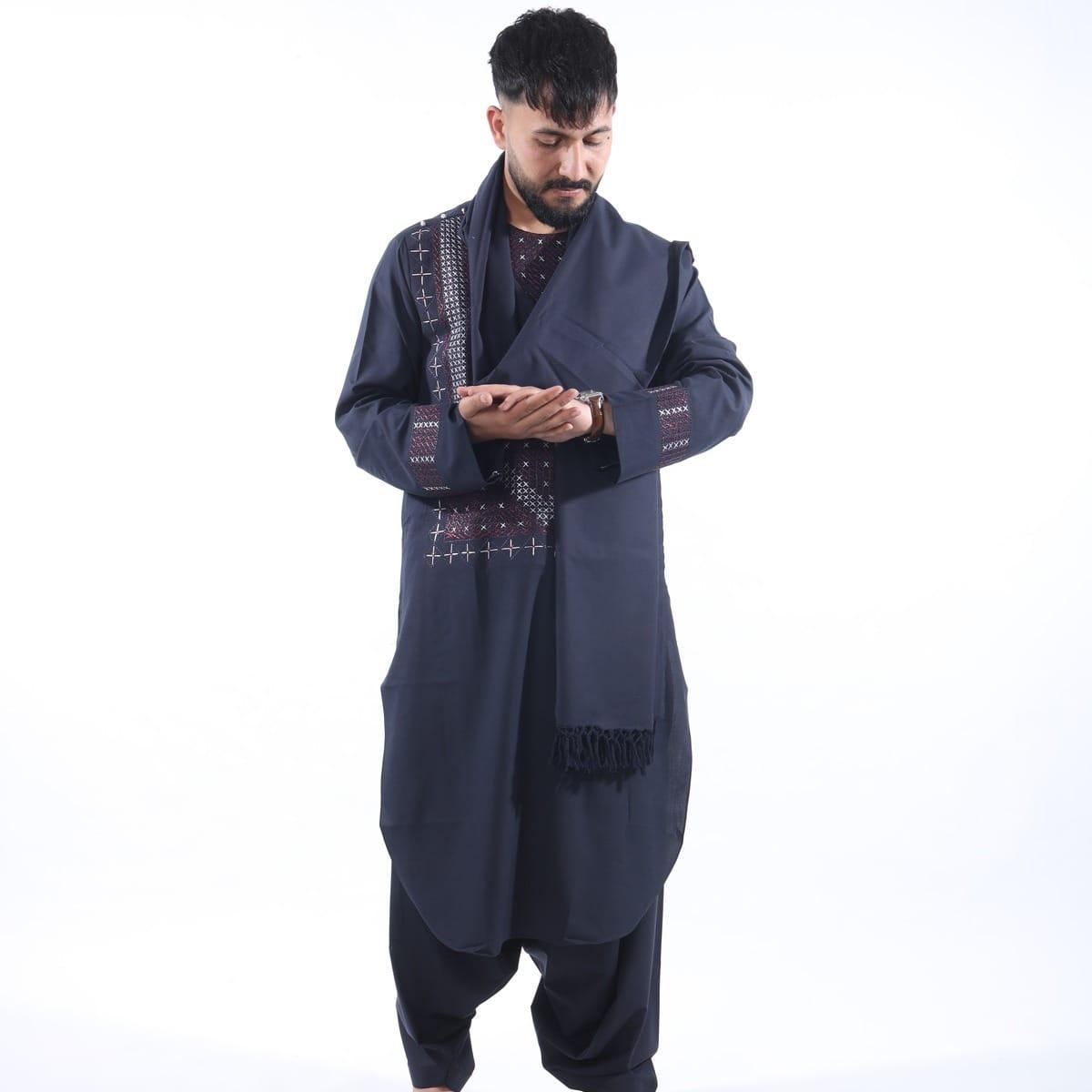 A man in a navy tunic and trousers with a checked woven shawl over his shoulders.