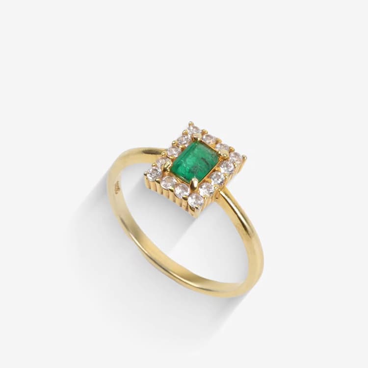 A gold ring set with a rectangular green emerald surrounded by small white stones.
