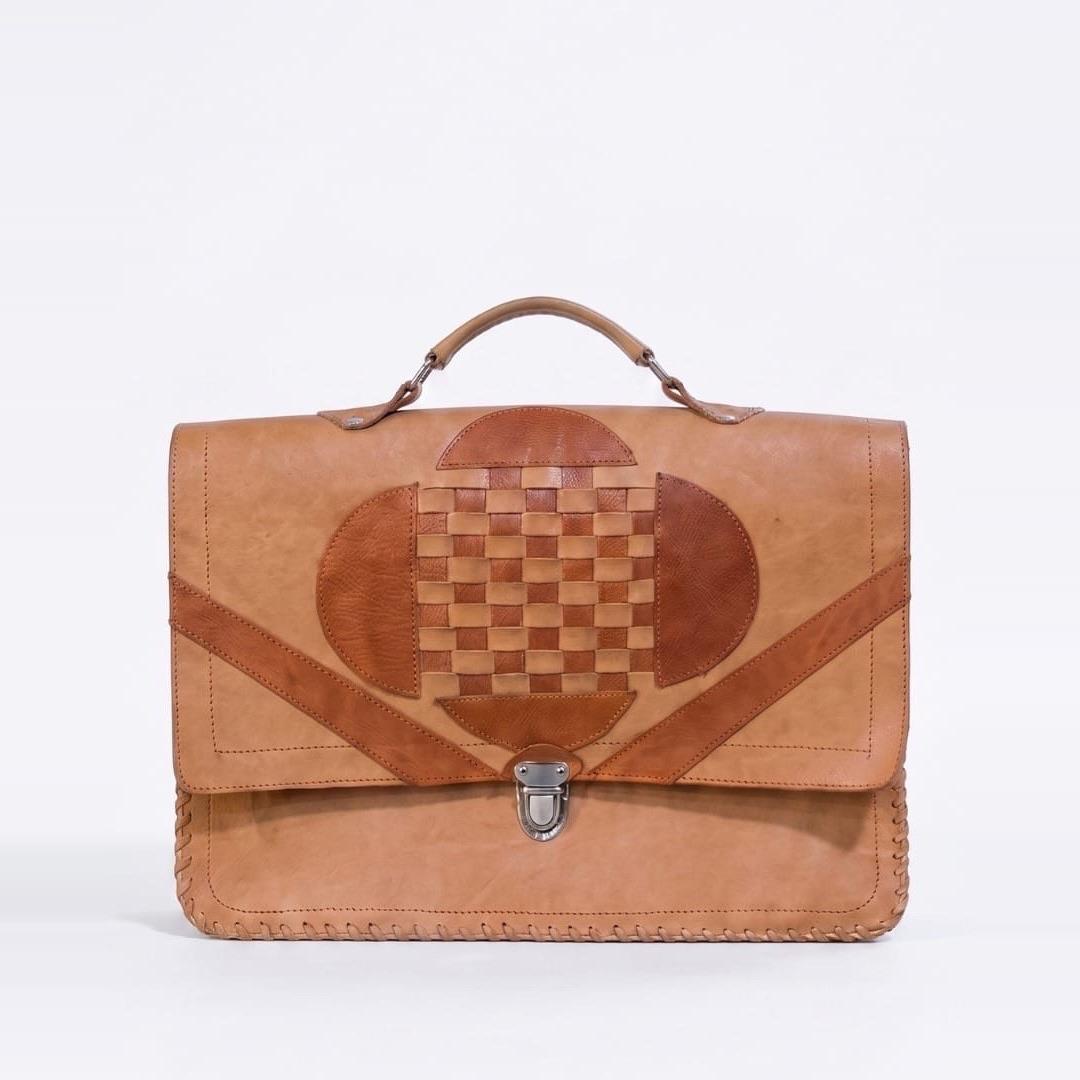 A tan leather satchel with a woven leather panel on the flap and a metal clasp.